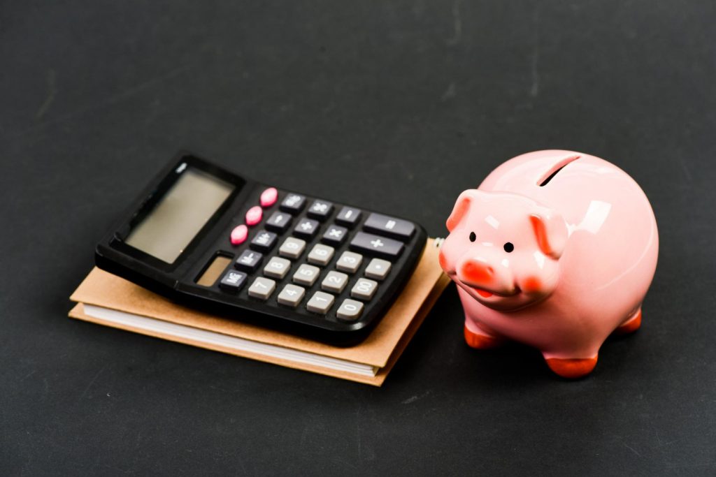 Une calculatrice posée à côté d'un cochon tirelire rose